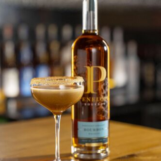Penespresso Martini in a brown sugar-rimmed coupe beside a Penelope Bourbon bottle